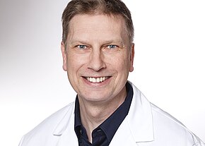 Jürgen Kloß Porträt eines lächelnden Mannes mittleren Alters in weißem Kittel vor hellem Hintergrund; Kopf-und-Schulteraufnahme, direkter Blick in die Kamera, freundlicher, professioneller Eindruck.