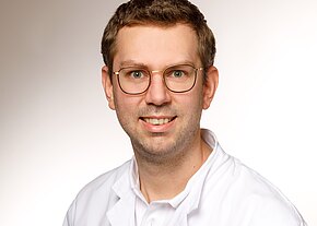 Dr. med. Hanno Zoske Porträt eines Mannes mit kurzer Frisur und Brille im weißen Kittel, freundlich lächelnd vor neutralem Hintergrund.