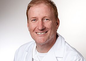 Dr. med. Stephan Brandt Porträt eines lächelnden Mannes mittleren Alters in weißem Kittel vor hellem, neutralem Hintergrund; wirkt wie medizinisches Personal.