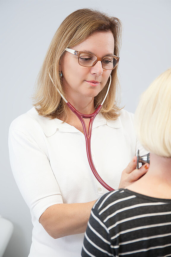 Ärztin hört mit Stethoskop den Brustkorb einer Patientin ab; ruhige medizinische Untersuchung in einer Praxis.